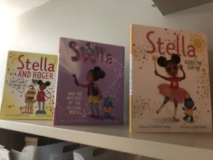 Three children's books by Clothilde Ewing are displayed upright on a shelf, each featuring a girl named Stella and colorful illustrations.