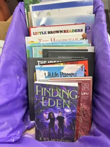 A purple container holds a collection of assorted children's and young adult books, with "Finding Eden" by K.R.S. McEntire at the front.