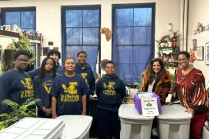 A group of students in St. Ethelreda Eagles shirts stands with two adults in an office, posing next to large plastic bins and a thank you box.